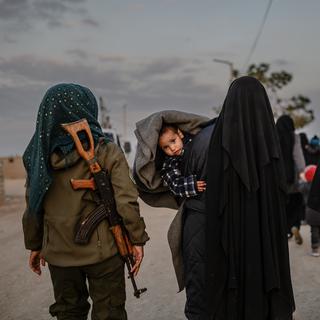 Des femmes, veuves du groupe Etat islamique, marchent dans le camp de Al-Hol sous la surveillance d'une combattante kurde. [AFP - Bulent Kilic]