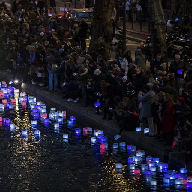 Un an après les attentats de Paris, des gens placent des lanternes colorées dans le Canal Saint-Martin, non loin de la Place de la République, le 13 novembre 2016. [Keystone/epa - Ian Langsdon]