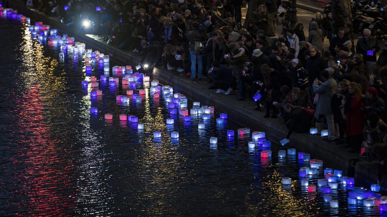 Un an après les attentats de Paris, des gens placent des lanternes colorées dans le Canal Saint-Martin, non loin de la Place de la République, le 13 novembre 2016. [Keystone/epa - Ian Langsdon]