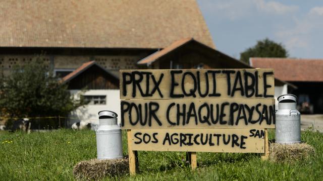 Une affiche installée dans un champ devant une ferme fribourgeoise pour protester contre le prix trop bas du lait. [Keystone - Jean-Christophe Bott]