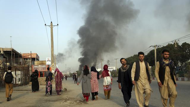 Des citoyens afghans marchent à proximité du Green Village, lieu de l'attentat et partiellement enflammé. [Keystone - Rahmat Gul]