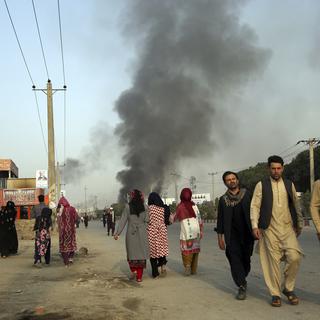 Des citoyens afghans marchent à proximité du Green Village, lieu de l'attentat et partiellement enflammé. [Keystone - Rahmat Gul]