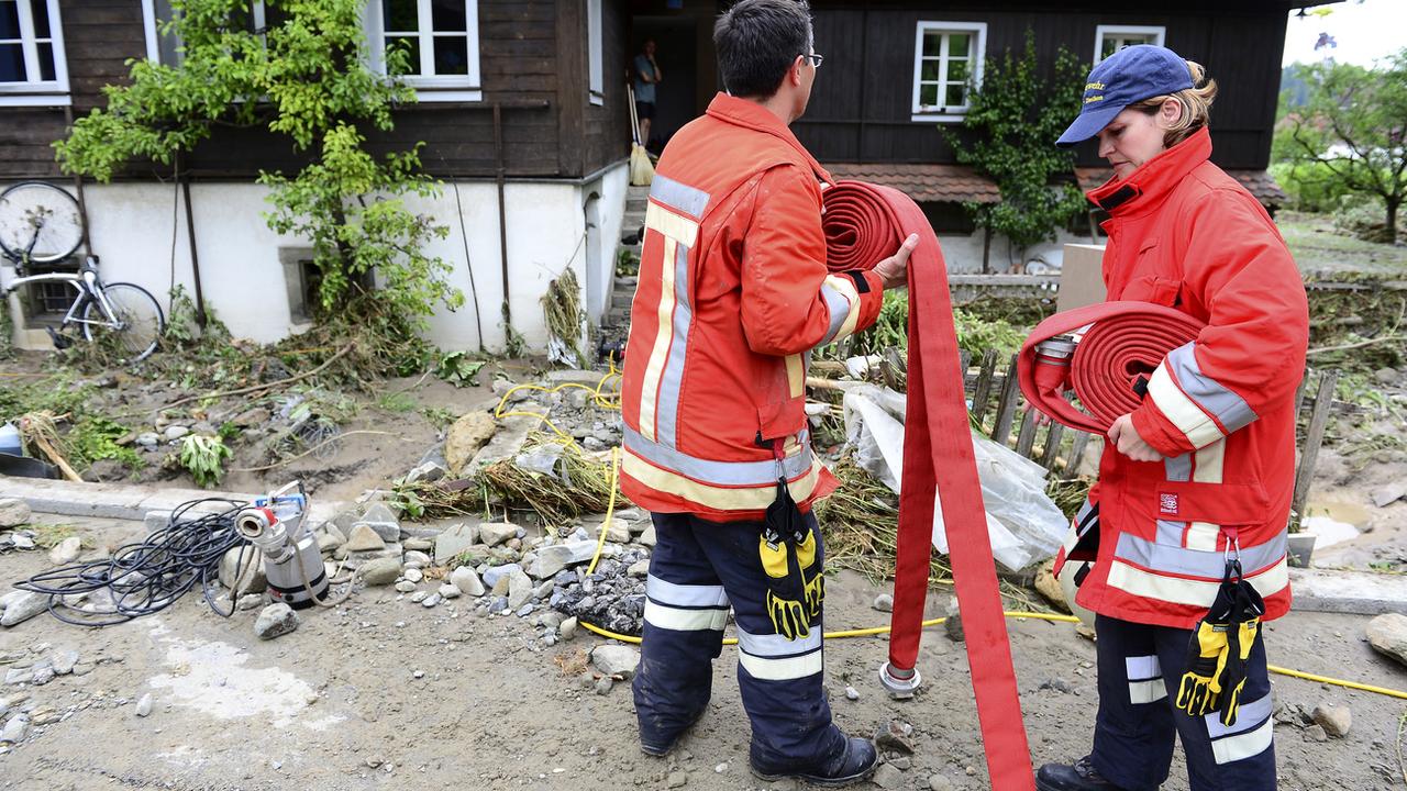 Deux pompiers sur les lieux d'une inondation à Dierikon (LU). [Keystone - Urs Flueeler]