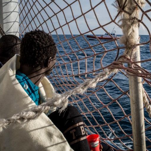 Des migrants à bord du navire Sea Watch 3, bloqués à bord depuis 12 jours, regardent un bateau des gardes-côte italiens. [AFP - Federico Scoppa]