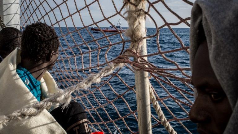 Des migrants à bord du navire Sea Watch 3, bloqués à bord depuis 12 jours, regardent un bateau des gardes-côte italiens. [AFP - Federico Scoppa]