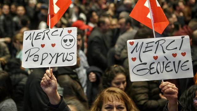 Une femme sans-papiers montre deux panneaux "Merci Papyrus" et "Merci Genève", lors de la séance de présentation du projet-pilote en février 2017. [Keystone - Salvatore Di Nolfi]