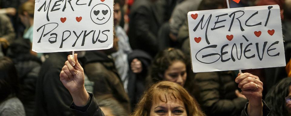 Une femme sans-papiers montre deux panneaux "Merci Papyrus" et "Merci Genève", lors de la séance de présentation du projet-pilote en février 2017. [Keystone - Salvatore Di Nolfi]