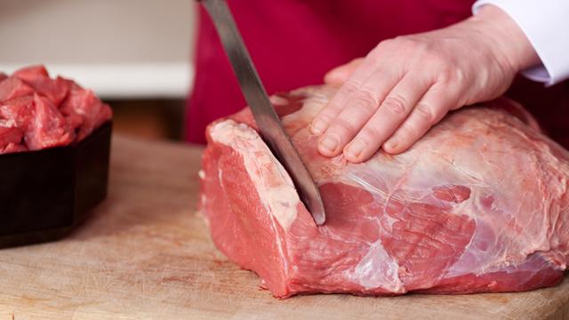 un boucher coupe la viande crue. [DepositPhotos]