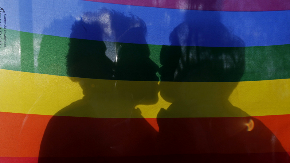 Un couple homosexuel s'embrasse derrière un drapeau aux couleurs arc-en-ciel (image d'illustration). [AP/Keystone - Dolores Ochoa]