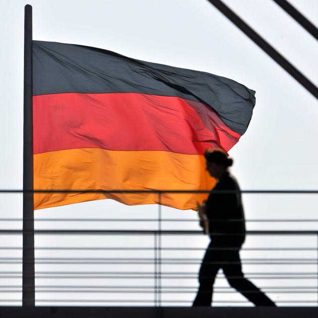 Des employés du Bundestag passent devant un drapeau allemand installé sur le Reichstag à Berlin. [Keystone - AP Photo/Gero Breloer]