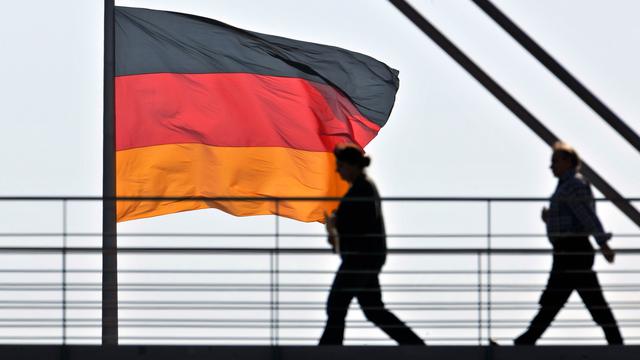 Des employés du Bundestag passent devant un drapeau allemand installé sur le Reichstag à Berlin. [Keystone - AP Photo/Gero Breloer]