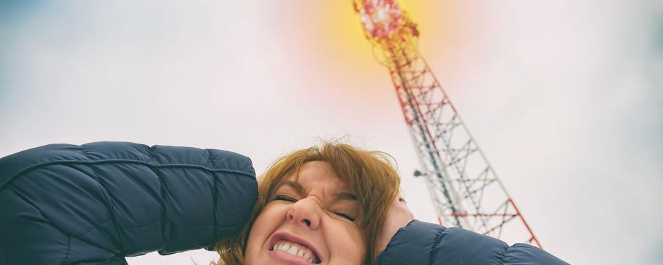 Une femme se tient la tête près d'une antenne émettrice de réseaux cellulaires. [Depositphotos - Amaviael]