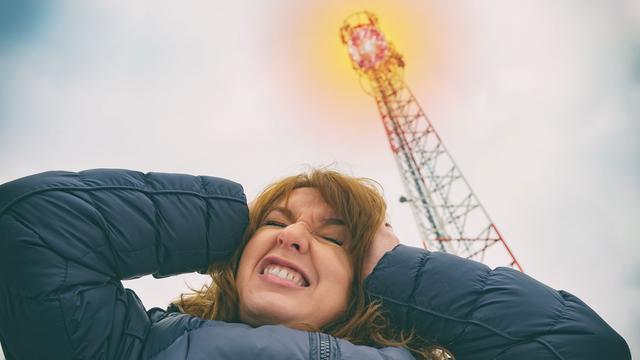 Une femme se tient la tête près d'une antenne émettrice de réseaux cellulaires. [Depositphotos - Amaviael]
