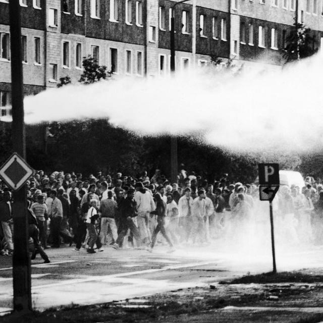 La police fait usage de canons à eau et de gaz lacrymogène contre des manifestants armés de pierres, barres et cocktails molotov à Rostock (ex-Allemagne de l'Est), le 23 août 1992. Les émeutiers, encouragés par la foule, s'en étaient pris aux logements de demandeurs d'asile. [KEYSTONE/AP Photo - Frank Hormann]
