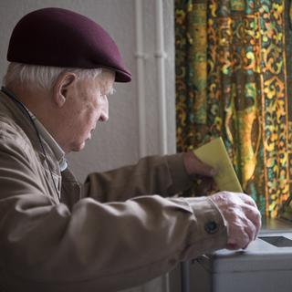 Un retraité glisse un bulletin dans une urne. [Anthony Anex - Keystone]