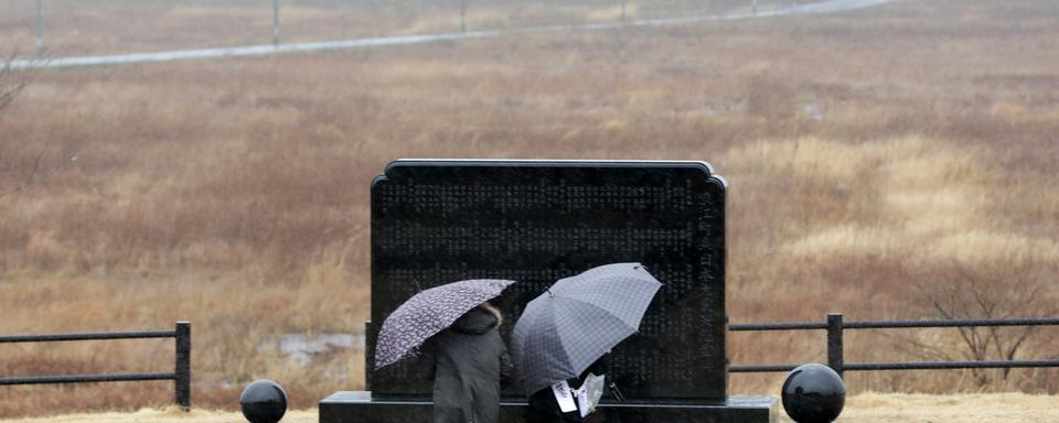 Deux personnes prient devant le mémorial de Fukushima, huit ans après le séisme meurtrier. [Keystone - EPA/Jiji Press Japan]