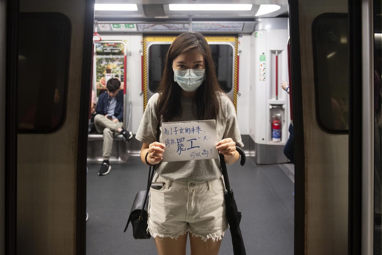 "Pour le bien du futur de nos enfants, pouvez-vous faire la grève pendant une journée?", dit la pancarte de cette manifestante, dans le métro de Hong Kong, le 5 août 2019. [Keystone/epa - Miguel Candela]