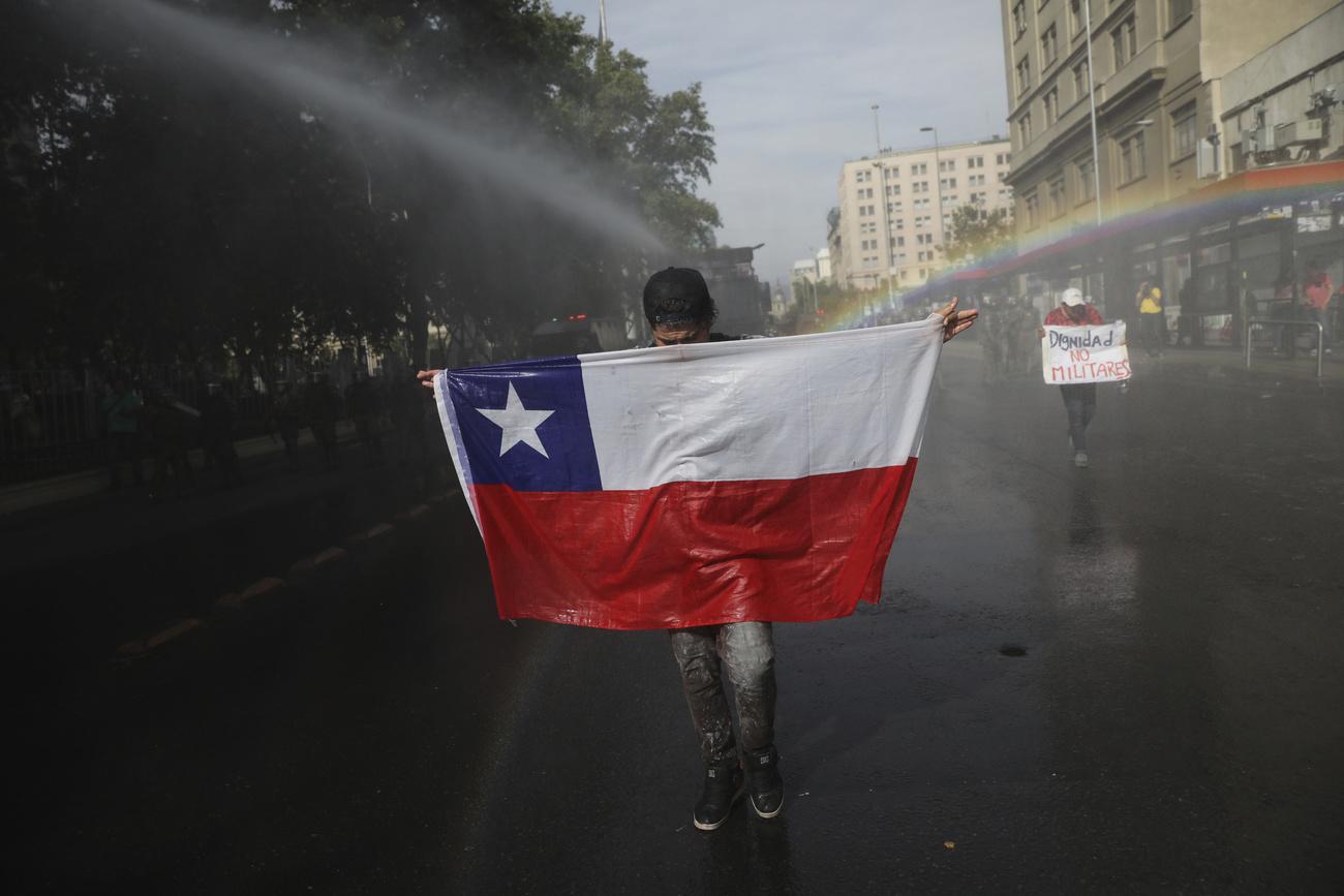 Un manifestant brandit un drapeau du Chili face aux canons à eau, dans la capitale Santiago, ce 26 octobre. [Keystone - Rodrigo Abd]