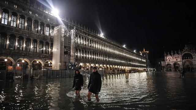 Des passants affrontent l'exceptionnelle "acqua alta" sur la place Saint Marc à Venise. [Marco Bertorello - AFP]