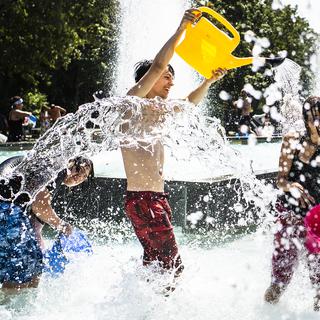 Des jeunes participent à une bataille d'eau dans la fontaine du parc de Milan à Lausanne. [Keystone - Jean-Christophe Bott]