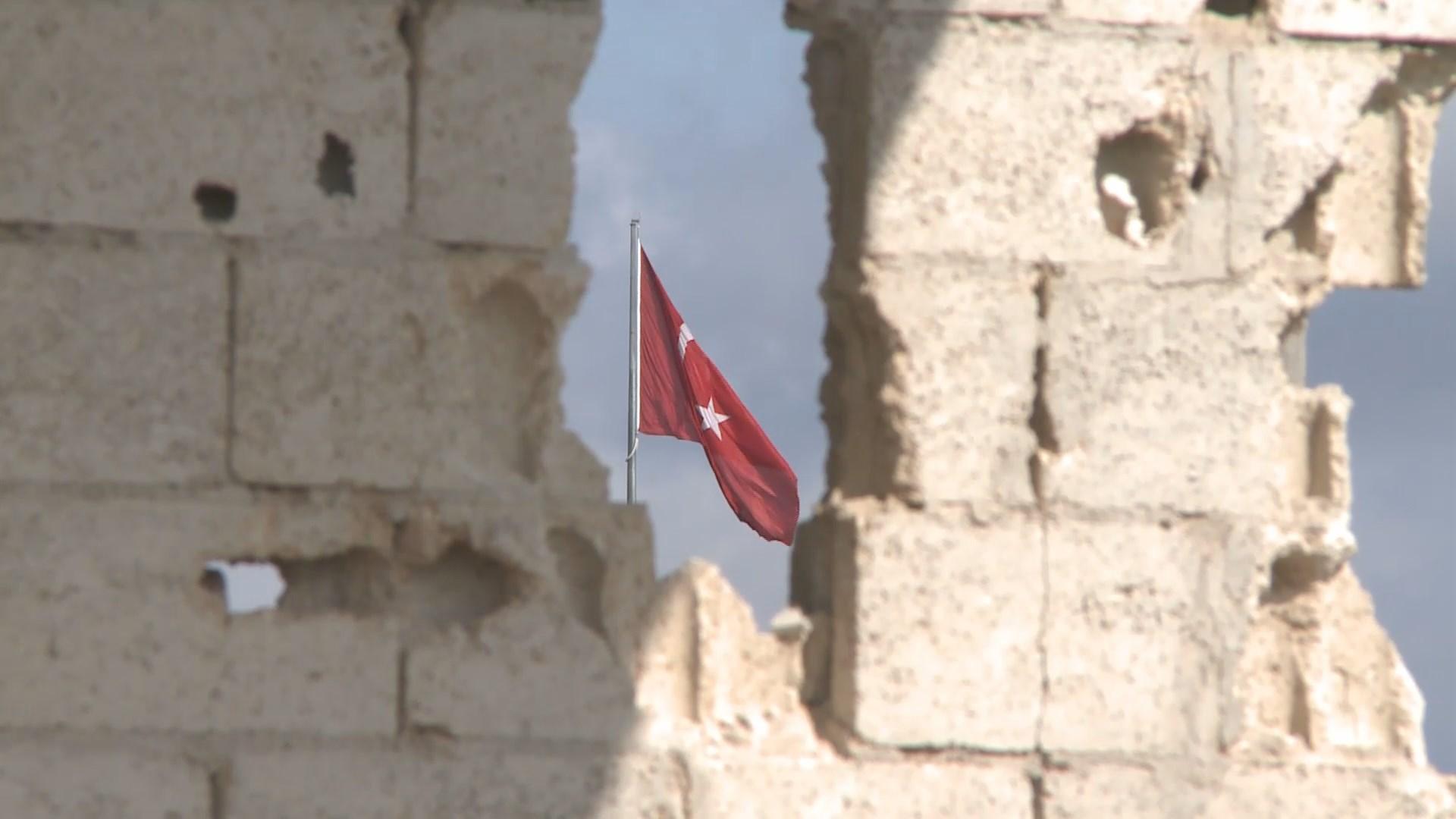 Le drapeau turc est visible au travers des murs en ruines à Kobé, à quelques mètres de la frontière avec la Turquie. [RTS]
