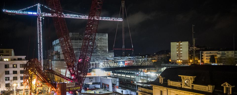 Une grue transporte le premier element de la passerelle "Rayon Vert" au-dessus des voies de la gare CFF de Renens. [Keystone - Jean-Christophe Bott]