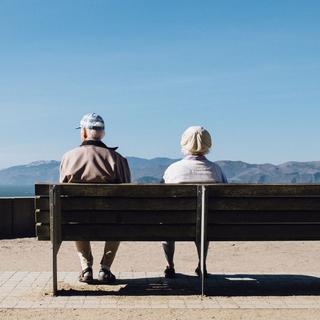 Un couple de seniors assis sur un banc regardent les montagnes. [Unsplash - Matthew Bennett]