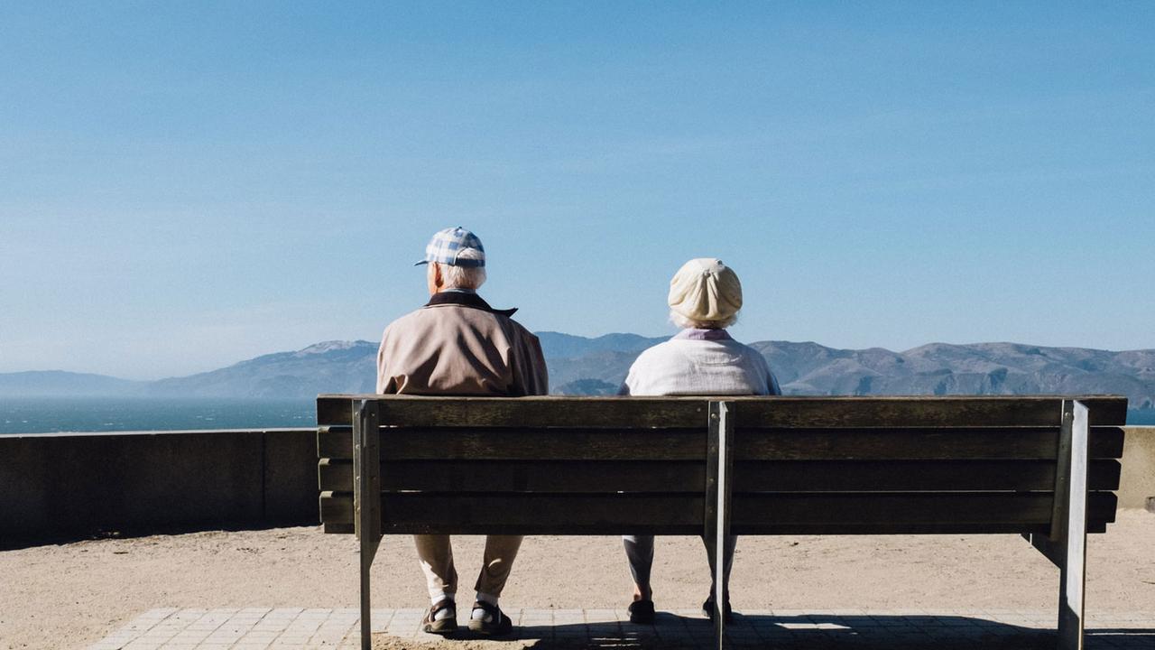 Un couple de seniors assis sur un banc regardent les montagnes. [Unsplash - Matthew Bennett]