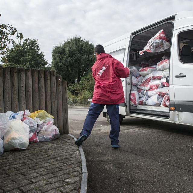 Une homme ramasse les textiles usagés pour Texaid. [Keystone - Christian Beutler]