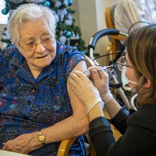 Une infirmière donne la première dose du vaccin anti-Covid à une résidente d'um EMS du canton de Fribourg, le 28 décembre 2020 à Cottens. [Keystone - Jean-Christophe Bott]