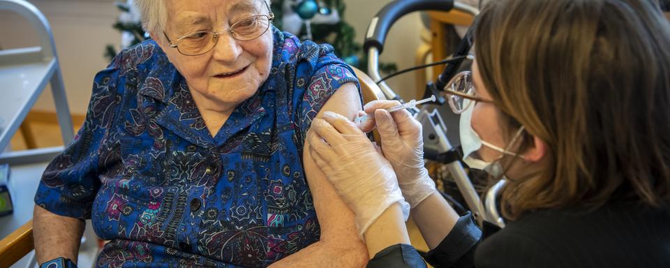 Une infirmière donne la première dose du vaccin anti-Covid à une résidente d'um EMS du canton de Fribourg, le 28 décembre 2020 à Cottens. [Keystone - Jean-Christophe Bott]