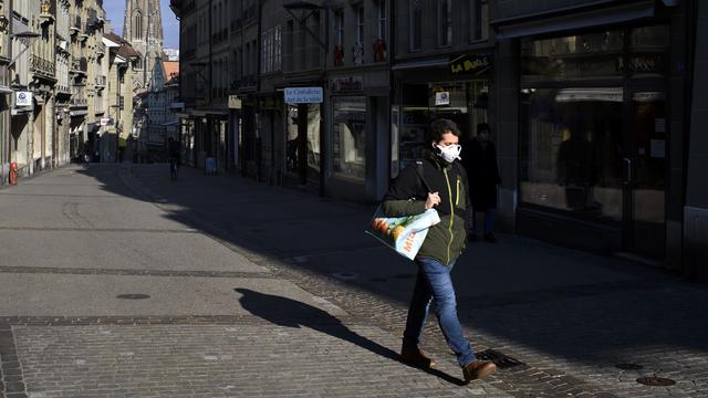 Un homme portant un masque marche dans la rue de Lausanne, ce mercredi 25 mars 2020 à Fribourg. [Keystone - Anthony Anex]