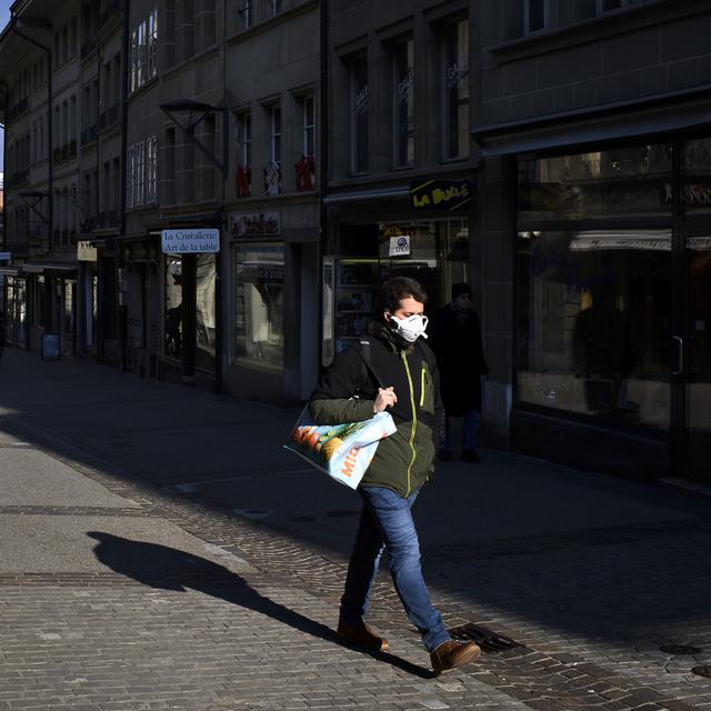 Un homme portant un masque marche dans la rue de Lausanne, ce mercredi 25 mars 2020 à Fribourg. [Keystone - Anthony Anex]