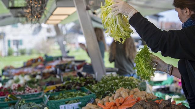 Une maraichere montre un legume a une cliente, ce samedi 21 mars 2020 a Puplinge pres de Geneve. En Suisse, l'interdiction des marches alimentaires en plein air touche directement les agriculteurs. Pour compenser, les maraichers trouver d'autres solutions pour vendre leurs produits, dont la vente directe a la ferme. (KEYSTONE/Martial Trezzini) [KEYSTONE - Martial Trezzini]