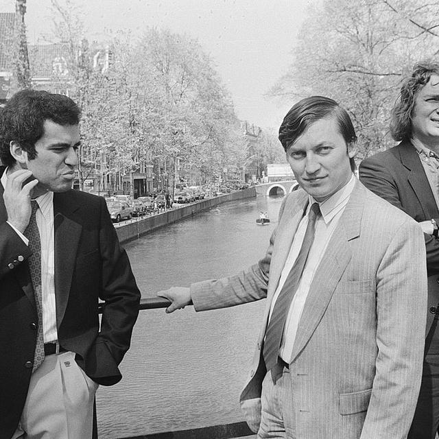 Gary Kasparov (à gauche) et Anatoli Karpov (au centre) à Amsterdam le 28 avril 1987 avec le joueur néerlandais Jan Timman (à droite). Les deux Soviétiques, plus grands joueurs de leur époque, disputèrent 144 parties dont 104 nulles, 21 victoires pour Garry Kasparov et 19 pour son rival Anatoli Karpov. [Nationaal Archief - Bart Molendijk / Anefo]