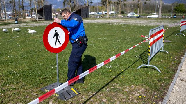 Un policier inspecte un panneau notifiant une restriction d'accès à la plage et aux Rives-du-lac à Yverdon le 9 avril 2020. [KEYSTONE - Jean-Christophe Bott]