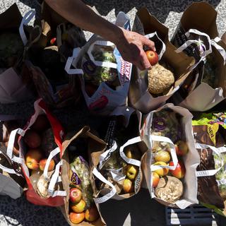 Des bénévoles de la structure "Le Point d'Appui" remplissent des sacs de nourriture avant de les donner aux personnes dans la précarité à l'occasion d'une distribution alimentaire lors de la crise du Coronavirus (Covid-19) le mercredi 20 mai 2020 à Lausanne. [Keystone - Jean-Christophe Bott]