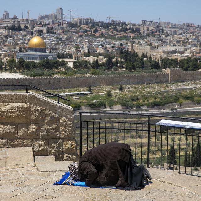 Vendredi 1er mai: une femme musulmane prie sur le Mont des oliviers à Jérusalem-Est, alors que la mosquée al-Aqsa, fermée pour cause de coronavirus, apparaît au loin. [Keystone - AP Photo/Ariel Schalit]