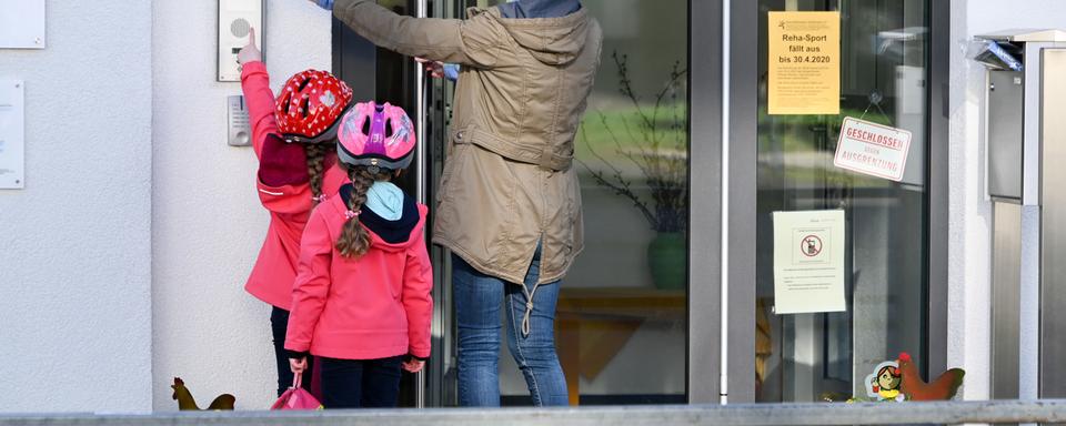 Une maman et ses deux filles à l'entrée d'une crèche, le 16 mars 2020. (image d'illustration) [KEYSTONE - Uwe Zucchi]