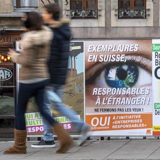 Des personnes passent devant des affiches pour les votations du 29 novembre, notamment l'initiative "entreprises responsables", le 14 novembre 2020 à Genève. [Keystone - Martial Trezzini]