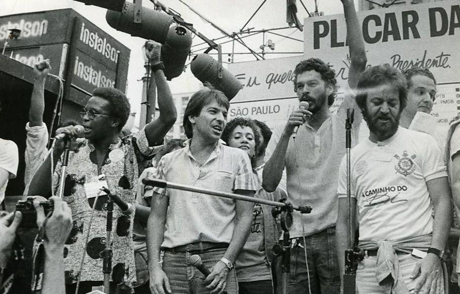 Le sociologue barbu Adilson Monteiro Alves (tout à droite sur la photo) lors d'une manifestation politique. Sócrates se trouve à sa droite avec le micro. [Capture d'écran du documentaire "Sur la route avec Sócrates" (2014)]