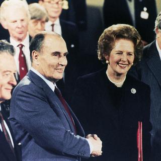 With the French and British Foreign Ministers at their side, French President Francois Mitterrand and British Prime Minister Mrs. Margaret Thatcher shake hands at a Canterbury Cathedral signing ceremony in 1986 which paved the way for the building and the operation of a tunnel between Britain and France beneath the English Channel. The signing of a treaty between the two nations was one of the legal steps required before work could commence on the project, first proposed nearly 200 years earlier in the time of Emperor Napoleon. (AP Photo/David Caulkin). [Keystone/AP Photo - David Caulkin]