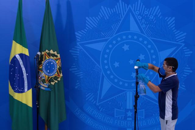 Un employé désinfecte le micro avant un discours de Jair Bolsonaro. Le président d'extrême-droite venait de rencontrer les gouverneurs du Brésil afin de définir des stratégies pour combattre le Covid-19 dans la ville de Brasilia. 23 mars 2020. [Keystone/epa - Joedson Alves]