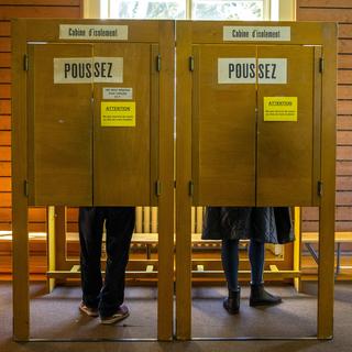 Des personnes remplissent leurs bulletins de vote dans les cabines d'isolements à Genève. [Keystone - Salvatore Di Nolfi]