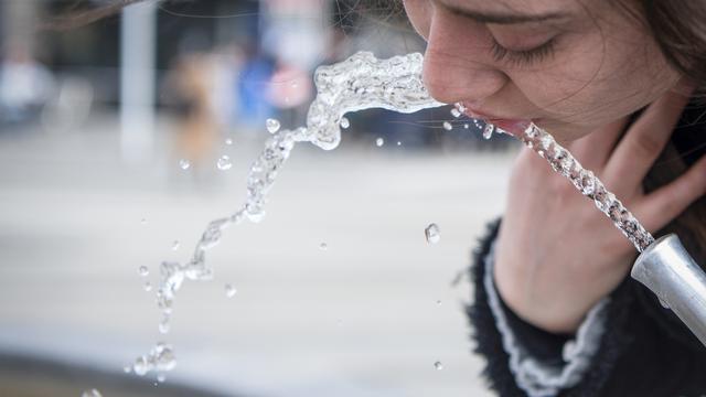 Une femme boit à une fontaine à eau, près du Paradeplatz à Zurich. [Keystone - Melanie Duchene]