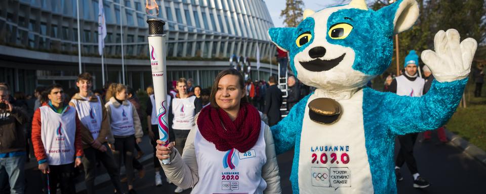 Yodli, la mascotte des JOJ 2020, pose en compagnie d'une relayeuse de la flamme olympique. [Jean-Christophe Bott]