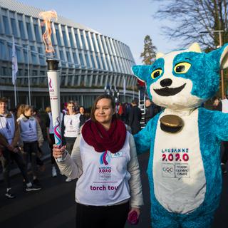Yodli, la mascotte des JOJ 2020, pose en compagnie d'une relayeuse de la flamme olympique. [Jean-Christophe Bott]
