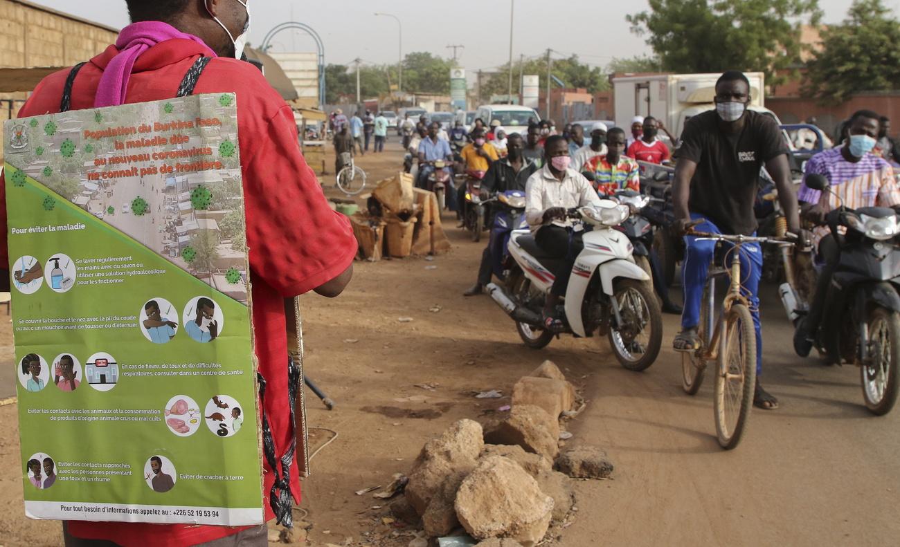 Un homme porte un panneau d'explications contre le coronavirus et donne un message de prévention grâce à un micro sur le bord d'une route, à Ouagadougou. Burkina Faso, le 30 mars 2020. [Keystone - EPA/STR]