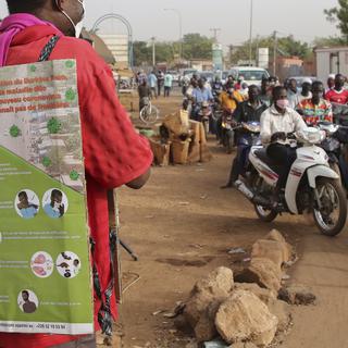 Un homme porte un panneau d'explications contre le coronavirus et donne un message de prévention grâce à un micro sur le bord d'une route, à Ouagadougou. Burkina Faso, le 30 mars 2020. [Keystone - EPA/STR]