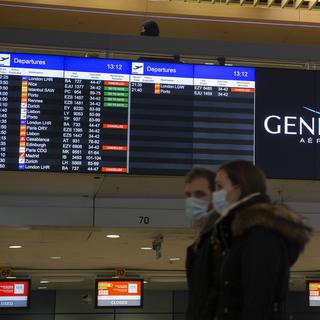 Des passagers à l'aéroport de Genève, devant des annonces de suppression de vols vers et depuis le Royaume-Uni et l'Afrique du Sud. [Keystone - Salvatore Di Nolfi]